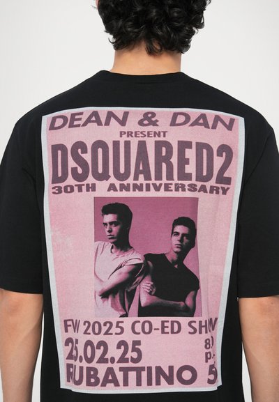 Črna majica s kratkimi rokavi z velikim rožnatim grafičnim tiskom na hrbtni strani, ki prikazuje besedilo in dve figuri. Oblika vključuje podatke o promocijskem dogodku.