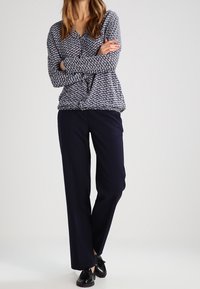 Cardigan a motivo navy con maniche lunghe e scollo a V, abbinato a pantaloni navy. La calzatura comprende scarpe nere. Texture liscia in tutta la superficie.