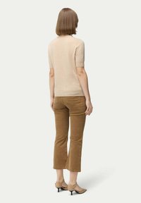 Beigefärgad kortärmad tröja med en slät textur, tillsammans med bruna kordflamsbyxor i ankellängd och ljusbruna klackskor.