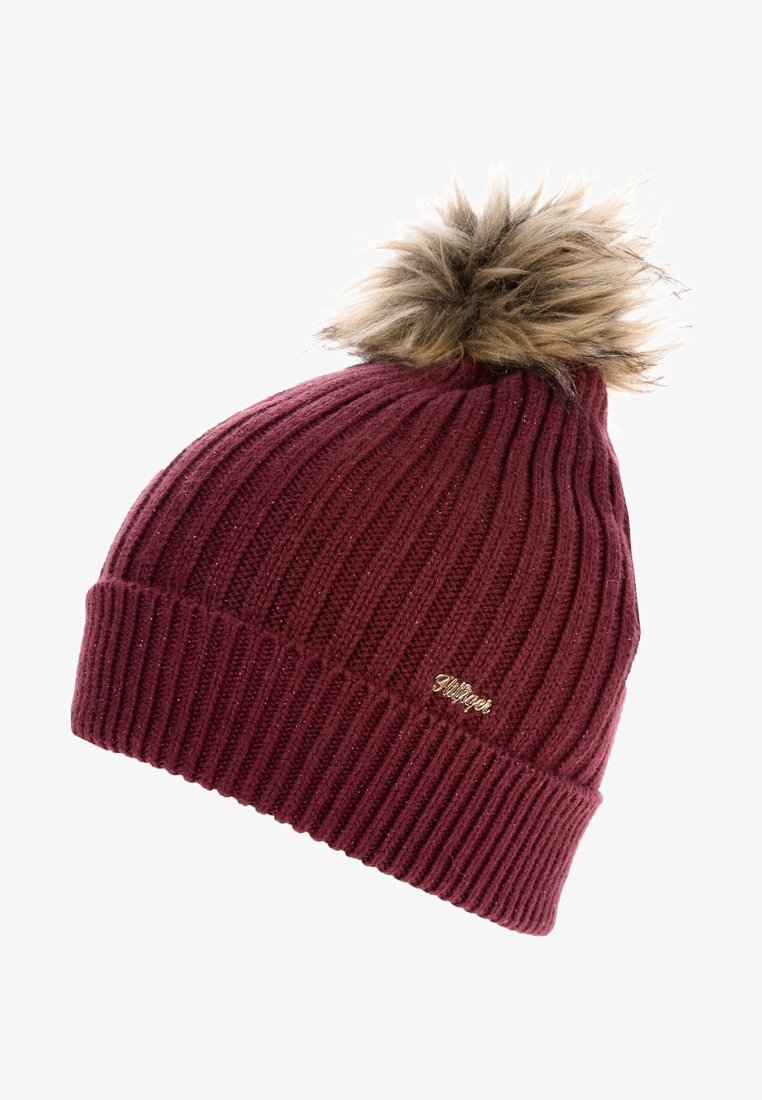 Bonnet en tricot côtelé bordeaux avec revers plié et pompon en fausse fourrure marron sur le dessus, avec un petit logo métallique de la marque.