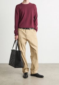 Burgunderfarbendes Langarmhemd, beigefarbene Hose, schwarzer Gürtel und schwarze Lederschuhe. Große schwarze Tragetasche mit geprägtem "HUGO." Einfaches, lässiges Outfit.