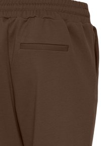 Pantaloni trening maro din stofă moale, cu talie elastică și un buzunar lateral discret. Textură netedă și croială structurată.