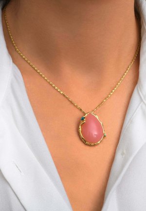 Collier chaîne en or avec un grand pendentif rose en forme de goutte et deux petites pierres turquoises porté sur le cou d’une personne au-dessus d’un vêtement blanc.