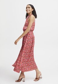 Abito lungo con motivi geometrici rossi e rosa, senza maniche, con una vita aderente, tessuto fluido e sandali con tacco a blocco trasparente.