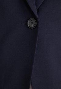 Marinblazer med en slät yta, enkel svart knapp med "BOSS"-logotyp och skräddarsydd passform som framhäver slagdesignen.