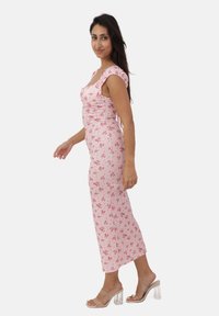 Różowa kwiatowa sukienka midi z krótkimi rękawami i marszczonymi detalami po bokach. Posiada dopasowany krój i jest zestawiona z przezroczystymi sandałami na obcasie.