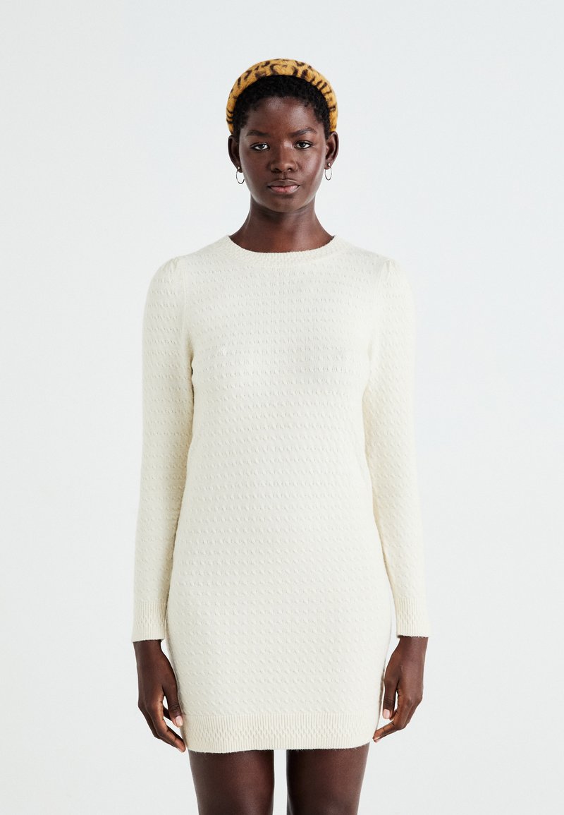Robe en tricot crème avec un motif texturé, manches longues, encolure ronde et ourlet côtelé. Matériau doux avec une silhouette près du corps.