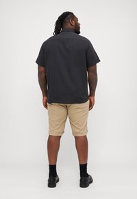 Chemise noire à manches courtes associée à un short beige. La chemise a une coupe droite, et le short est de longueur genou avec des ourlets retroussés. Chaussures noires.