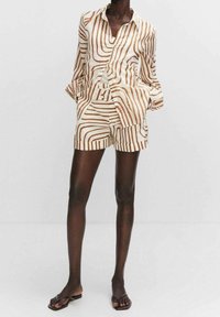 Set di maglietta a righe e pantaloni corti in beige e marrone. La maglietta presenta un colletto e maniche lunghe; i pantaloni corti hanno una vestibilità rilassata e tasche.