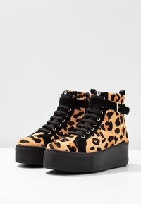 Leopardikuosis korkeavartiset tennarit mustilla mokkanahkaosilla, joissa on paksu pohja ja kultaiset rei'ät nauhoille. Mukana säädettävä hihna.