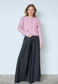 Rožinė tweedo švarkelis su apvaliu iškirpimu, priekiniu kišenių ir aukso spalvos sagomis, derinamas su aukšto liemens plačiomis juodomis kelnėmis.