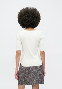 Witte top met korte mouwen en een brede halslijn, gecombineerd met een gestructureerde, meerkleurige rok tot op de knieën met een geweven patroon.