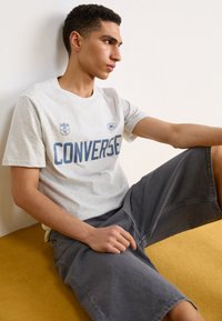 Heled hallist puuvillane T-särk, millel on tumehallis "CONVERSE" tekst, sisaldades logode detaile. Komplektis tumehallid lühikesed püksid. Lihtne disain ja lõige.