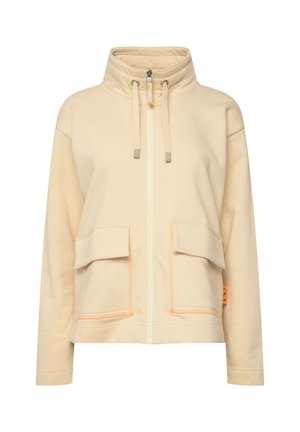 Giacca beige con zip e collo alto, due tasche frontali, dettagli arancioni e tessuto morbido. Presenta lacci per una vestibilità regolabile.