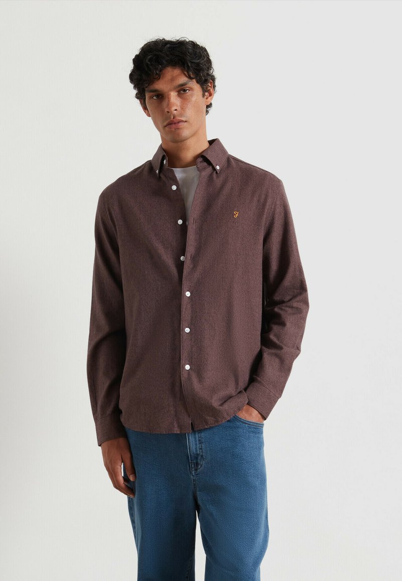 Camicia marrone a pulsante con una trama sottile e cuciture a contrasto, con bottoni bianchi e un logo ricamato sul petto.