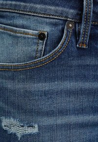 Jeans i denim med en urblekt blå färg och lätt slitage. Synlig sömnad i brunt och svarta metallaccenter vid midjan.