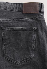 Back pocket and waistband of black denim jeans with a brown leather patch label reading "DENIM SUPPLY."