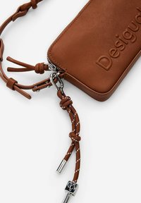 Brauner Leder-Zippouch mit geprägtem Logo, verstellbarem Riemen und gemusterten Kordelakzenten sowie Details aus Silbermetall.