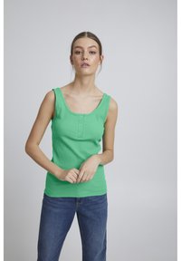 Grøn, ribbet tanktop med brede stropper og en scoop-udskæring. Har tre knapper foran og en tætsiddende silhuet. Bæres sammen med blå jeans.