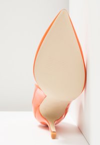 Chaussure à talon haut orange avec bout pointu et finition brillante. Dotée d'un talon fin et d'une semelle beige lisse. Design simple et élégant.