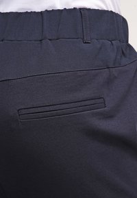 Pantalons bleu foncé en tissu lisse, dotés d'une taille élastique et d'une seule poche arrière avec un design de fente horizontale.