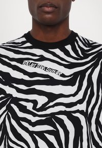 Svart og hvit t-skjorte med zebra-striper og rund hals; har en "Versace Jeans Couture" logo i hvitt foran.