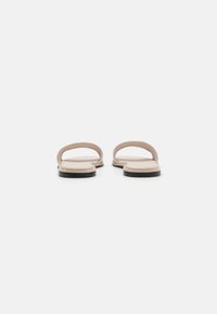 Pantofle na slip-on s měkkým, světle růžovým koženým svrškem, plochou černou podešví a minimalistickým designem s dvěma tenkými popruhy přes nárt.