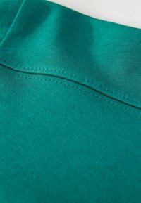 Nahaufnahme eines türkisfarbenen Stoffes, der detaillierte Nähte und eine glatte, gestrickte Textur zeigt.