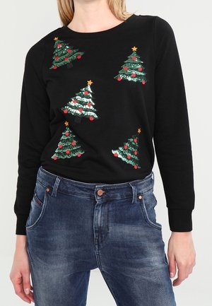 Czarna koszula z długim rękawem z pięcioma zielonymi choinkami ozdobionymi czerwonymi bombkami i złotymi gwiazdkami na szczycie, noszona z niebieskimi dżinsami.