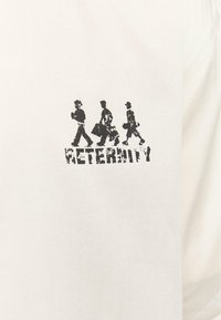 Tricou alb din bumbac cu un imprimeu grafic negru reprezentând patru figuri care merg și cuvântul "ETERNITATE" scris cu un font uzat dedesubt.