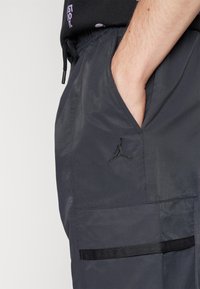Dark gray cargo shorts made from lightweight fabric, featuring a side pocket, elastic waistband, and an embroidered logo accent.