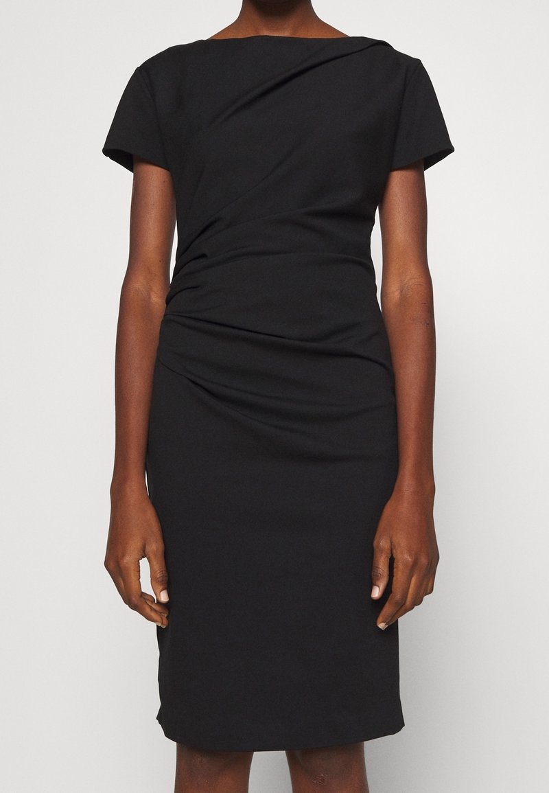 Czarna sukienka z gładkiego materiału. Ma skręcony fason w okolicy biustu, krótkie rękawy i dopasowaną sylwetkę.