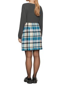 Grijze long-sleeve top met een aansluitende silhoeet, gecombineerd met een geruite rok in blauw, wit en zwart, vervaardigd uit een textuurstof. Zwarte schoenen.