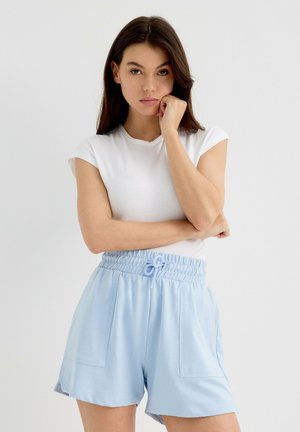 Pantalones cortos de color azul claro hechos de tela suave, con cinturilla elástica y cordón de ajuste, que presentan dos bolsillos frontales, combinados con una camiseta blanca ajustada.