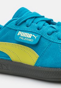 Sinine sametist kets, millel on kollased aksessuaarid ja paelad. Omab musta tekstuuriga tallat ning bränditud keelekleebi, mis ütleb "PUMA PALERMO".