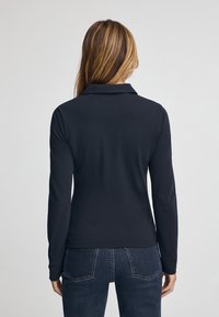 Polo de manga larga azul marino con cuello, presenta una textura suave y una silueta ajustada. La vista posterior muestra un diseño liso sin detalles adicionales.