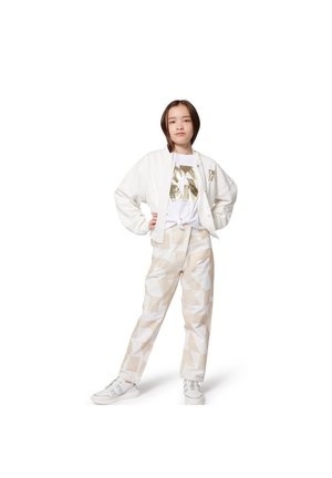 Chaqueta bomber blanca con pantalones de crema y beige con estampado. La camiseta presenta un gráfico metálico dorado. Un par de zapatillas blancas completa el atuendo.