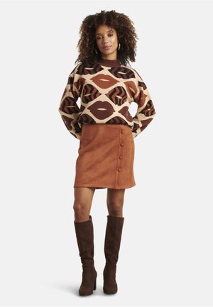 Sweater in bruin en beige met lippen en dierenpatronen; roestkleurige suède rok met knoopdetails; kniehoge bruine laarzen.
