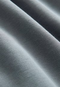 Szary, teksturowany materiał o miękkiej, żłobionej powierzchni. Materiał ma gładkie wykończenie i delikatne krzywizny, podkreślające jego elastyczną naturę.