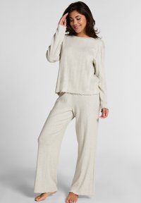 Lichtbeige loungewear set bestaande uit een lange mouw top met een ronde hals en zachte, textuurstof. De broek heeft een wijde pijp met ruwe zomen.