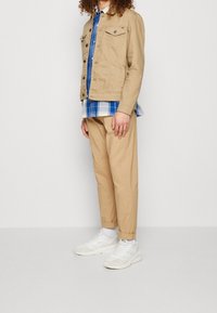 Brązowa dżinsowa kurtka, niebieska koszula w kratę pod spodem oraz brązowe zwężane spodnie. Białe trampki dopełniają strój. Prosty wzór i luźny krój.