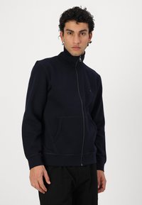 Navy zip-up sweatshirt in soft fabric with a high collar, side pockets, and contrast stitching detail. Simple, relaxed-fit design.