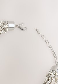 Silver metallic clutch with bead detailing, a rounded closure, and a detachable chain strap. Smooth texture with sparkling accents.