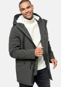 Grå isoleret parka med fleece-foret hætte, knap- og lynlåslukninger samt sidelommer, båret over en struktureret hvid sweater.