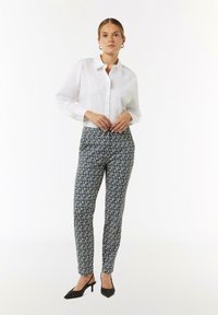 Witte blouse, gebloemde blauwe broek en zwarte hakken. Bloemmotief op de broek, gladde stof. Rechte pasvorm, taps toelopend ontwerp.