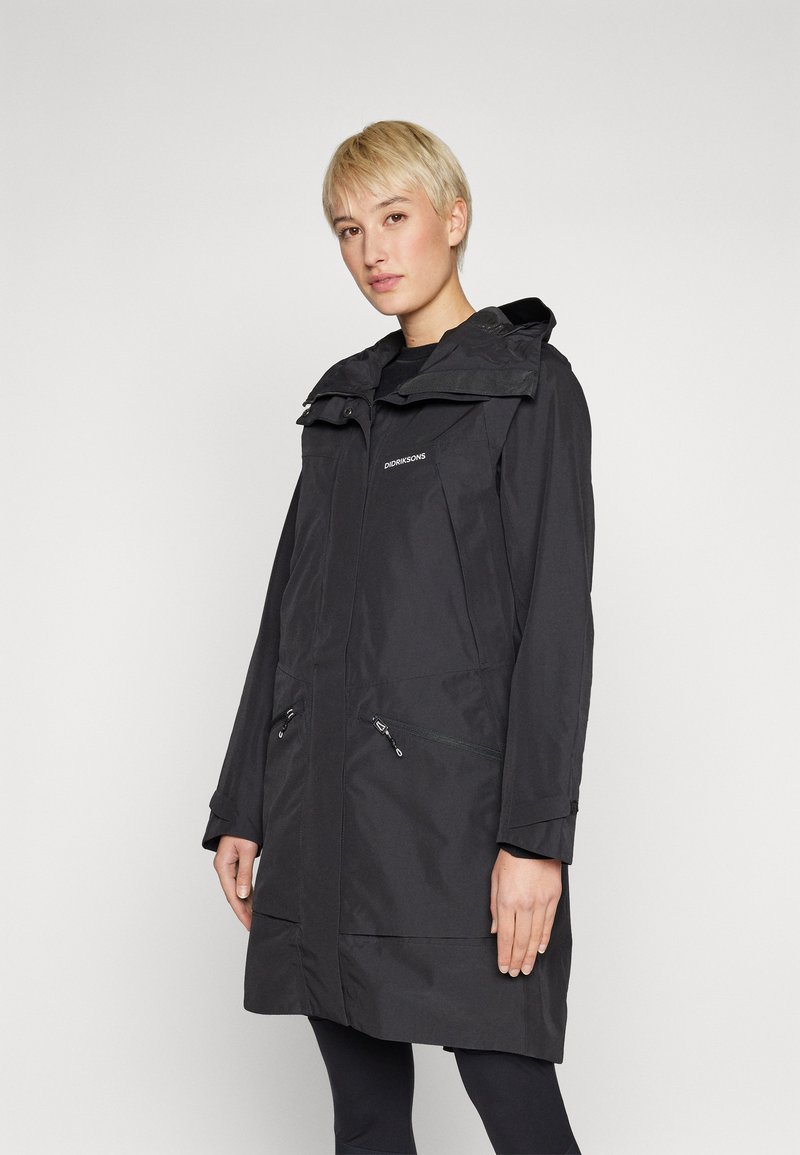 Svart vanntett frakk med hette, to frontlommer med glidelås, og kne-lengde design. Minimalistisk stil med en jevn tekstur.