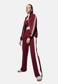 Atletiekoutfit in bordeaux, met een ritsjack met witte strepen en bijpassende strakke broek, van gladde stof en een relaxte pasvorm.