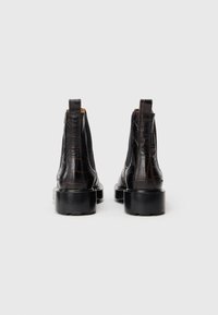Botas de tobillo de cuero negro con un patrón texturizado de cocodrilo, puntera redonda y suela de goma negra gruesa. Cuenta con dos tiradores en la parte trasera.