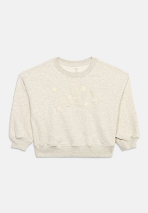 Lyst beige kort genser med puffermer som går til trekvart lengde og subtilt GAP-logo brodert med små hvite blomster på forsiden.