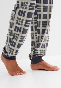 Pantaloni da pigiama da uomo in un mix di cotone, con un motivo a quadri in blu navy, grigio e bianco, con polsini aderenti blu navy. Piedi scoperti su uno sfondo bianco.